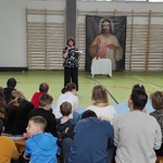 Nauczycielka mówi do uczniów siedzących na łąweczkach