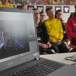 Slajd wyświetlany na ekranie. obok uczniowie biorący udział w lekcji on-line