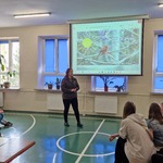 Pani leśnik omawia slajd wyświetlany na ekranie.Uczniowie siedzą na ławeczkach.