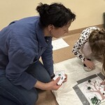 Uczennica siedząc na podłodze przesuwa palcem pompon na odpowiednie miejsce