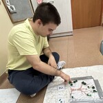 Uczeń siedząc na podłodze przesuwa palcem pompon na odpowiednie miejsce