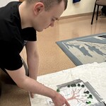 Uczeń siedząc na podłodze przesuwa palcem pompon na odpowiednie miejsce
