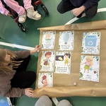 Uczniowie siedzą wokół szarego arkusza papieru z naklejonymi obrazkami