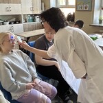 Nauczyciel w przebraniu lekarza mierzy temperaturę uczniowi