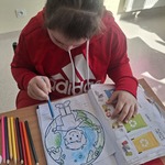 Uczennica siedzi przy stoliku i koloruje obrazek