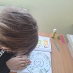 Uczennica siedzi przy stoliku i koloruje obrazek