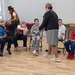 Nauczycielka idzie w kierunku uczniów siedzących na krzesłąch