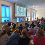 Społeczność szkolna siedzi na ławkach i ogląda film wyświetlany na ekranie