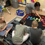 Uczniowie siedzą na podłodze, czytają napis: mama