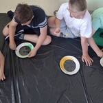 Uczniowie siedzą na podłodze, wykonują pracę plastyczną.