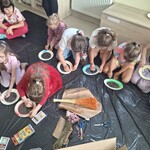Uczniowie siedzą na podłodze, wykonują pracę plastyczną.