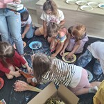 Uczniowie siedzą na podłodze, wykonują pracę plastyczną.