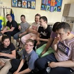 Uczniowie siedzą na podłodze i na krzesłach