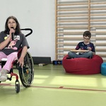 Uczennica na wózku śpiewa do mikrofonu, Z tyłu uczeń gra na cymbałkach