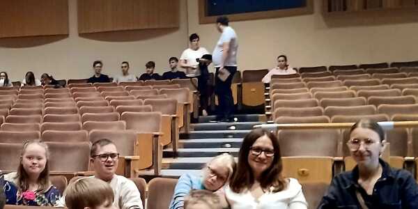 Uczniowie z opiekunami siedzą w fotelach na auli.