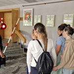 Prowadzący stoi na scenie z dwiema paniami ze służb mundurowych i zaprasza do obejrzenia audycji  muzycznej.