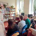 Emerytowana nauczycielka czyta książkę uczniom siedzącym na krzesłach