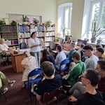 Emerytowana nauczycielka czyta książkę uczniom siedzącym na krzesłąch