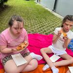 Uczennice siedzą na kocu i jedzą pizzę