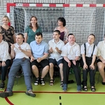 Absolwenci siedzą na krzesłach. Za nimi stoją wychowawczynie