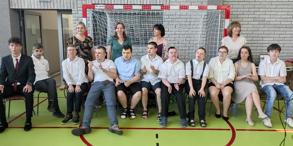 Absolwenci siedzą na krzesłach. Za nimi stoją wychowawczynie
