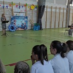 Pani dyrektor mówi do społeczności szkolnej siedzącej na ławkach