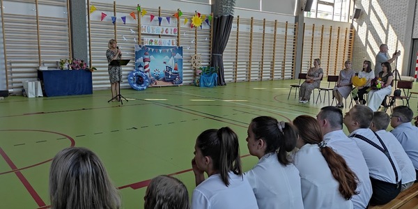 Pani dyrektor mówi do społeczności szkolnej siedzącej na ławkach