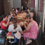 Uczestnicy półkolonii w restauracji siedzą przy stołach i jedzą gofry