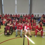 Społeczność szkolna w czerwonych ubraniach siedzi na trybunach na sali gimnastycznej
