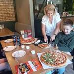 Nauczycielka kroi pizzę. Wokół stołu siedzą uczniowie