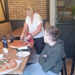 Nauczycielka kroi pizzę. Obok siedzi solenizant