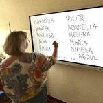 Nauczyciel pisze na tablicy interaktywnej imiona uczniów.