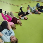 Grupa uczniów leży na plecach z podniesionymi nogami na podłodze