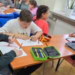 Uczniowie siedzą przy stoliku i rysują na kartkach