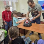Prowadzący warsztaty trzyma torebkę z biały proszkiem na wulkanem stojącym na ławce. Obok stoi uczennica i nauczycielak