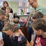 Prowadzący warsztaty i uczniowie stoją wokół stołu. Jeden uczeń zagląda do pudełka