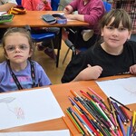 Uczennice siedzą przy stole i rysują na kartkach
