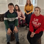 Grupa uczniów i nauczycielka siedzą w holu muzeum