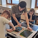 Jeden uczeń wykonuje kolagrafię, koledzy obserwują jego pracę
