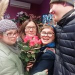 Uśmiechnięta trójka uczniów oraz wychowawczyni trzymająca bukiet róż na tle wystawy  w kwiaciarni