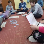 Uczniowie siedzą na dywanie. Przed uczniami leżą książki do komunikacji.