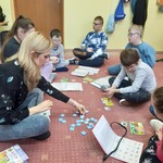Nauczyciel i uczniowie siedzą na dywanie. Nauczyciel pokazuje uczniom symbole.