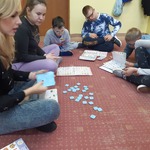 Nauczycielka i uczniowie siedzą na dywanie. Przed nimi leżą książki do komunikacji.