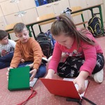 Uczniowie siedzą na dywanie i otwierają swoje książki komunikacyjne
