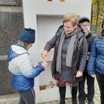 Nauczycielka zapala znicz trzymany przez uczennicę w ręku.