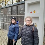 Dwie uczennice trzymające się za ręce stoją na tle kolumbarium.