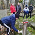 Nauczycielka i troje uczniów przygląda się uczennicy stawiające znicz na grobie.