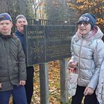 Grupa uśmiechniętych uczniów stoi obok tablicy z napisem Cmentarz Wojskowy