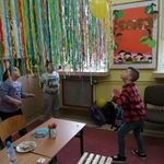 Troje uczniów odbija balon nad sznurkiem z kolorową dekoracją z pasków bibuły.