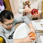 Dwie dziewczynki stoją przy umywalce. Dziewczynka w okularach myje jabłko pod kranem. Druga dziewczynka patrzy na jabłko trzymane w dłoniach.